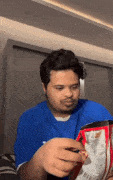 a man in a blue shirt is holding a bag of chips in his hands .