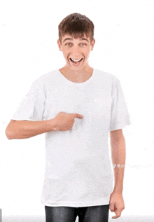 a young man wearing a white t-shirt is pointing to his chest