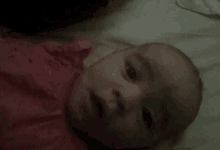 a baby is laying on a bed with a pink shirt on and looking at the camera .