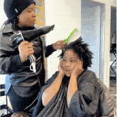 a woman blow drying another woman 's hair with a black hair dryer
