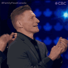 a man in a suit applauds in front of a blue background with the letters cbc on the bottom