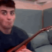 a man is playing a guitar and making a funny face while sitting on a couch .