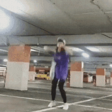 a person is dancing in a parking garage with a purple shirt on .
