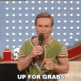 a man in a green shirt is holding a microphone and saying up for grabs