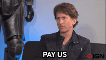 a man sitting on a couch with the words pay us above him