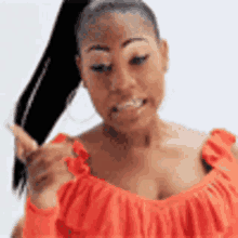the woman is wearing a red off the shoulder top and holding her hair in a ponytail .