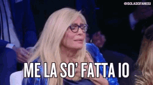 a woman wearing glasses and a blue jacket is sitting in a crowd and says me la so ' fatta io .
