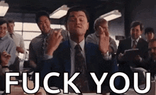 a man in a suit and tie is giving a middle finger in front of a group of people .