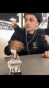 a young man wearing headphones is sitting at a table with a carton of awesome milk