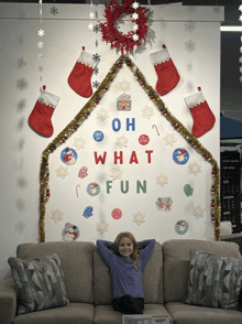 a little girl is sitting on a couch in front of a wall that says oh what fun