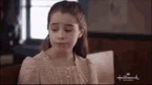 a young girl is sitting at a table with a book and making a sad face .