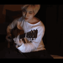 a young man is playing an acoustic guitar in a dark room
