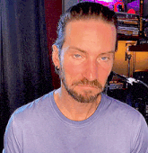 a man with a beard and earrings is wearing a blue shirt