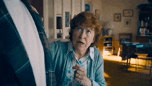 an elderly woman in a blue sweater is talking to a man in a suit in a living room .