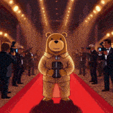 a teddy bear is standing on a red carpet surrounded by people