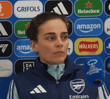 a woman wearing an arsenal jacket stands in front of various logos