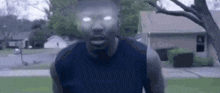 a man in a blue tank top is standing in front of a house with glowing eyes .
