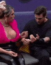 a man and a woman are sitting on a couch and the woman is wearing a pink top