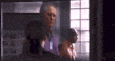a man in a purple shirt is standing in front of a window in a dark room .