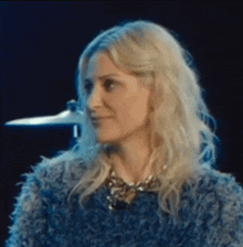 a woman with blonde hair is wearing a blue furry jacket and a necklace .