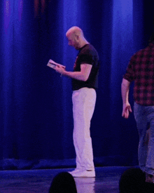 a man wearing a black shirt that says shoot whip holds a book