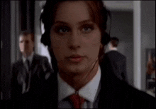 a woman wearing headphones and a tie looks at the camera
