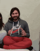 a man wearing a hoodie that says nike sits on a bed