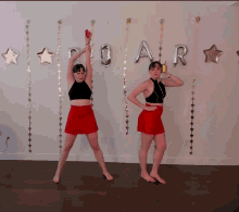 two women are dancing in front of a wall with roar balloons hanging from it