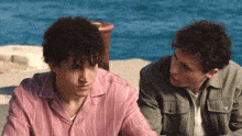 a man in a pink striped shirt stands next to another man in a green jacket