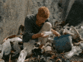 a man is kneeling down in a pile of trash looking at something