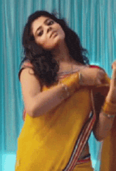 a woman wearing a yellow saree is dancing in front of a blue curtain .