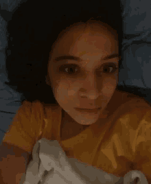 a woman in a yellow shirt is laying in bed with a white blanket