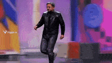 a man in a black leather jacket is walking on a stage
