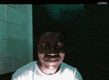 a man in a white shirt is smiling in a dark room with luma written on the bottom right