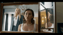 a woman in a white tank top looks at herself in a mirror