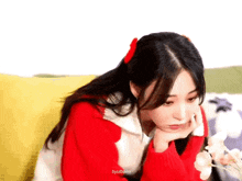 a girl wearing a red sweater is sitting on a couch with her hand on her chin .