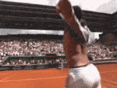 a man without a shirt is standing on a tennis court with his arms in the air