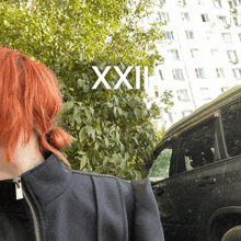 a woman with red hair is standing in front of a building with xxi written on the bottom