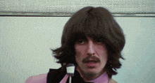 a man with long brown hair and a mustache is wearing a pink shirt and tie
