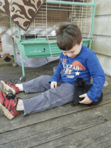 a young boy wearing a blue shirt that says " dream big " is playing with a black rabbit