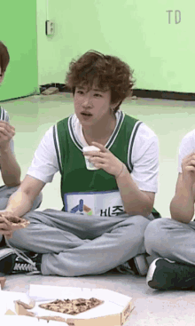 a young man sitting on the floor eating pizza and wearing a shirt that says hlz