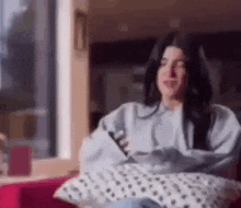 a woman is sitting on a couch with a pillow and looking at her phone .