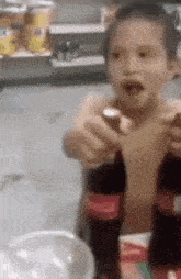 a young boy is sitting at a table holding a bottle of coca cola .