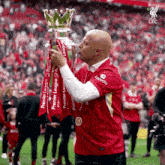 a man in a red shirt with the word expedia on it kisses a premier league trophy