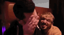 two men are laughing and covering their faces with their hands while sitting next to each other in a dark room .