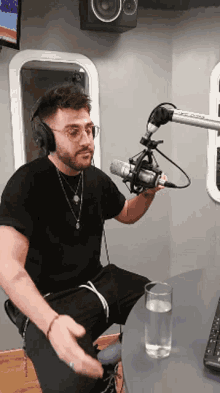 a man wearing headphones is sitting in front of a microphone with a glass of water in front of him