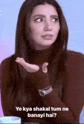 a woman in a brown turtleneck is making a funny face and holding her hand up .