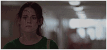 a woman in a green shirt stands in a dark hallway