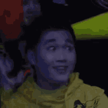 a man in a yellow hoodie is making a funny face while sitting in a dark room .
