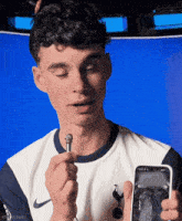 a man in a tottenham shirt holds a microphone and a cell phone